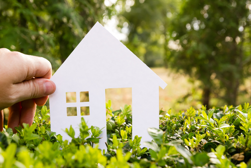 Hand,Holding,White,Paper,House,Against,Green,Background.,Real,Estate